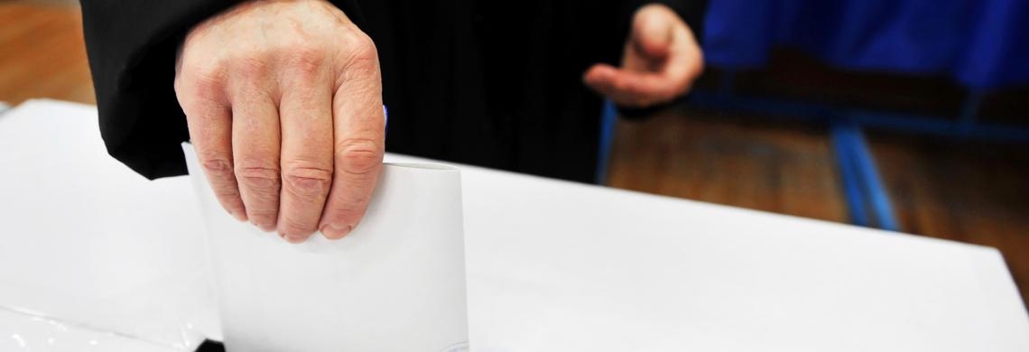 Person, die einen Zettel in die Urne wirft.